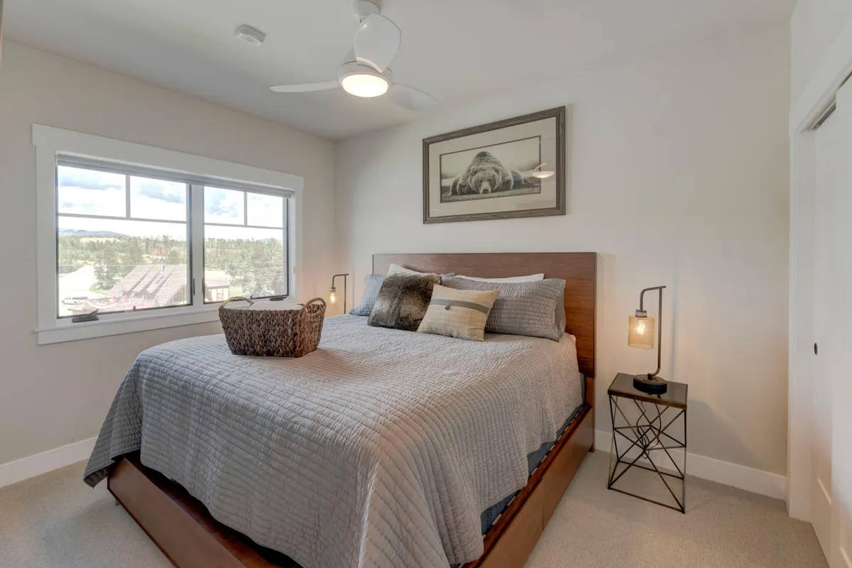 A serene bedroom with a plush queen bed, soft bedding, ample natural light streaming in through large windows, tasteful artwork, and a cozy nightstand. The calming color palette and comfortable furnishings create a restful retreat.