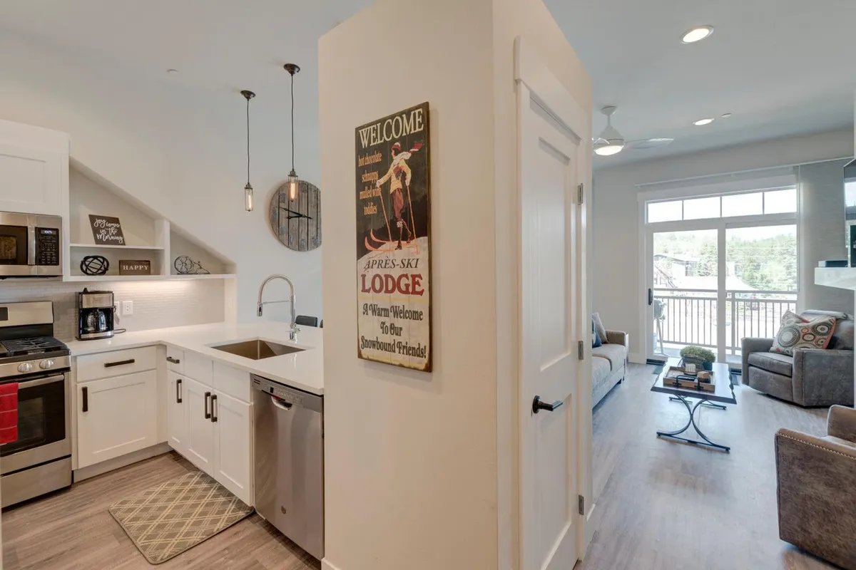 This image presents the open kitchen area with a clear view of the living room seating and welcome sign, featuring large windows that bring in natural light. The scene conveys a sense of comfort, warmth, and family-friendly togetherness, with ample space for group cooking, socializing, and relaxing after a day out.