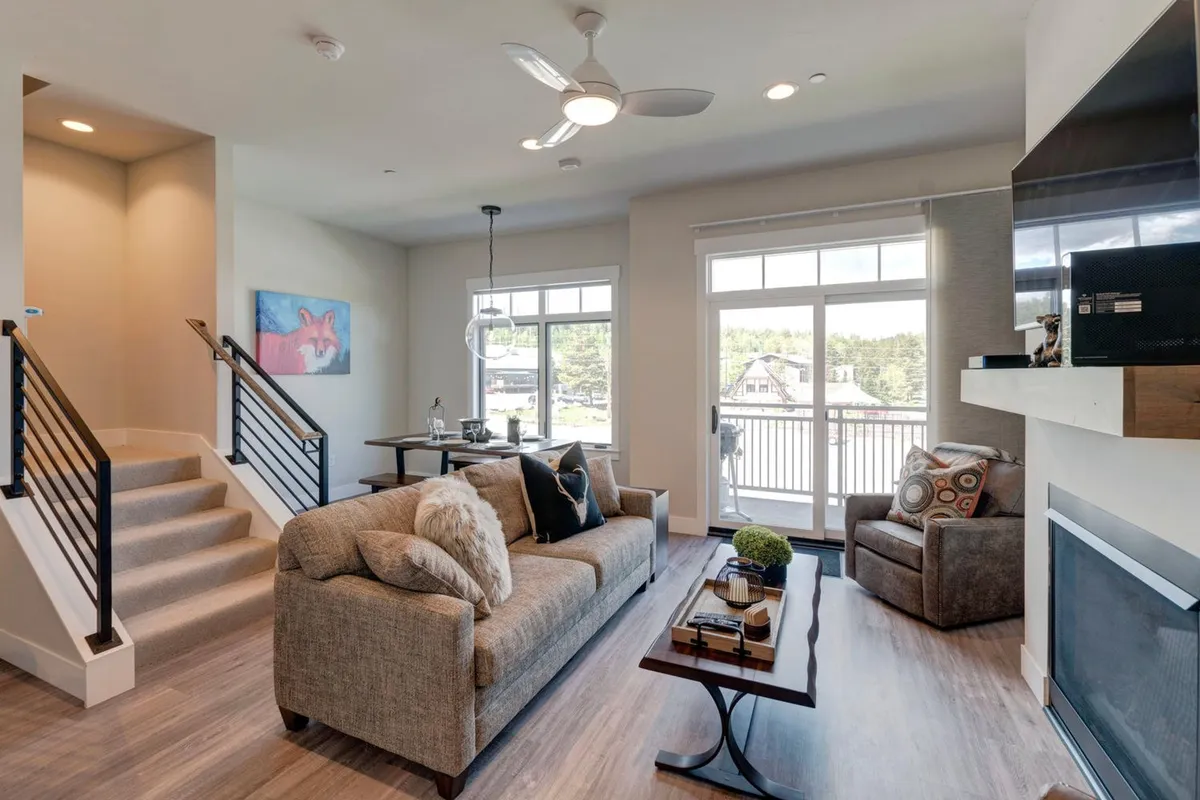 A welcoming living area with a comfortable sofa, coffee table, artwork on the wall, a staircase, and large windows. The mood is relaxed and inviting, ideal for family gatherings or unwinding after a day of adventure.