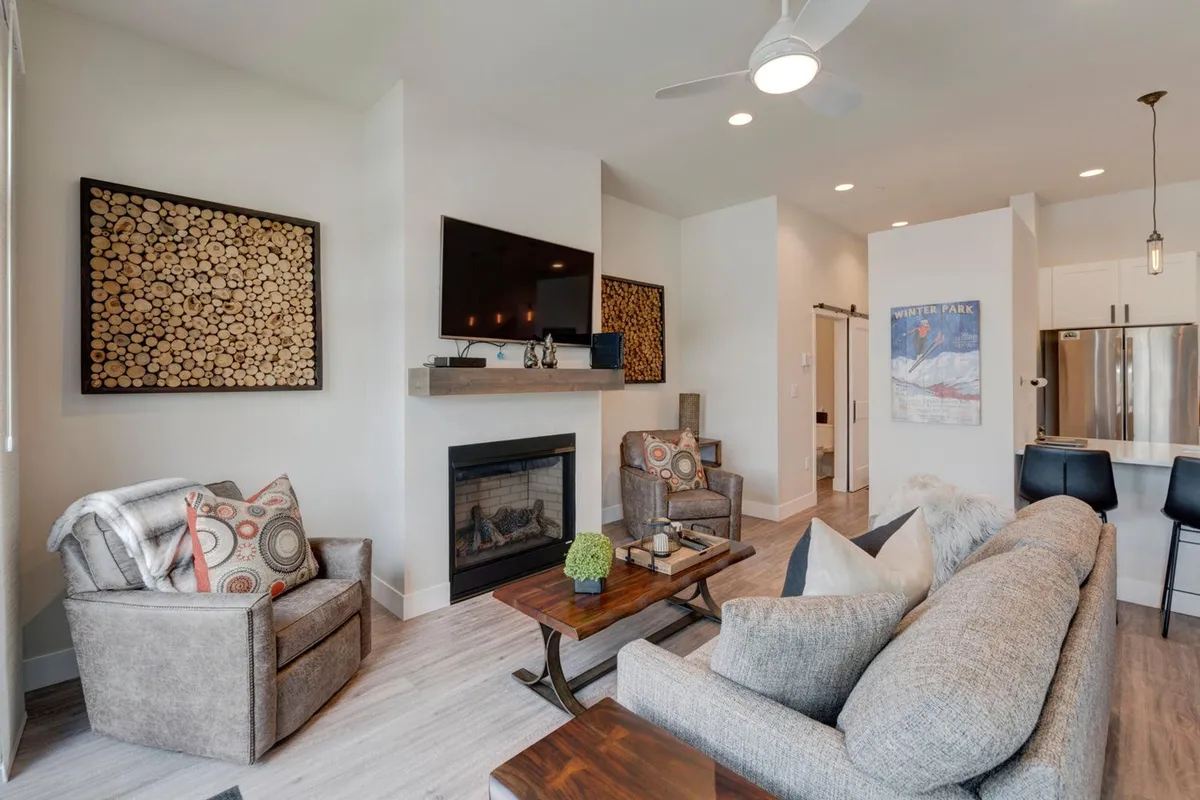 This cozy living room features a fireplace, comfortable sofa, coffee table, and tasteful artwork. The inviting setup encourages gathering, playing board games, or unwinding as a family, echoing the warmth and hospitality promoted in the section.