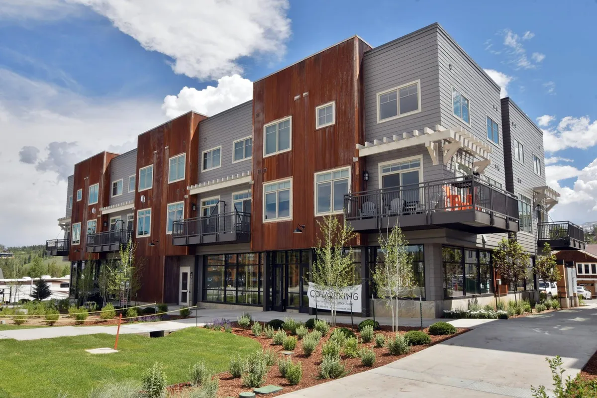 Modern, multi-level building exterior featuring balconies and a landscaped garden. The photo is taken at sunset, capturing a lively community ambiance and highlighting the building’s architectural style and outdoor gathering spaces.