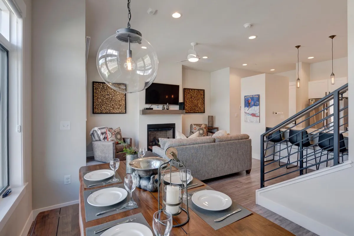 This image showcases a welcoming living and dining area, featuring a comfortable sofa, a cozy fireplace, artwork on the walls, and a dining table set for a meal. The space is bathed in natural light, emphasizing the open-concept layout and inviting atmosphere.