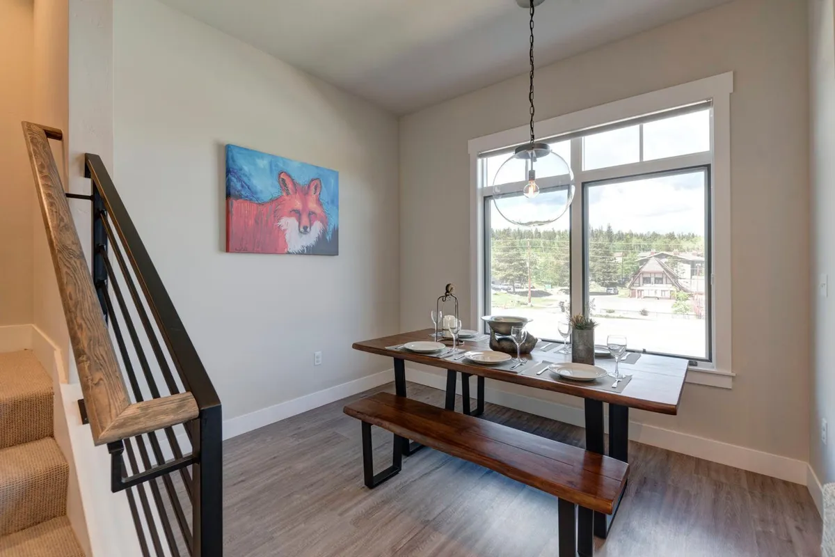 A bright dining area featuring a communal table set under a large window, with a whimsical fox painting adding charm. The scene hints at both productivity and leisure, with plenty of natural light and open space ideal for working remotely, casual meetings, or enjoying meals. The window view subtly connects the interior with the surrounding mountain setting.