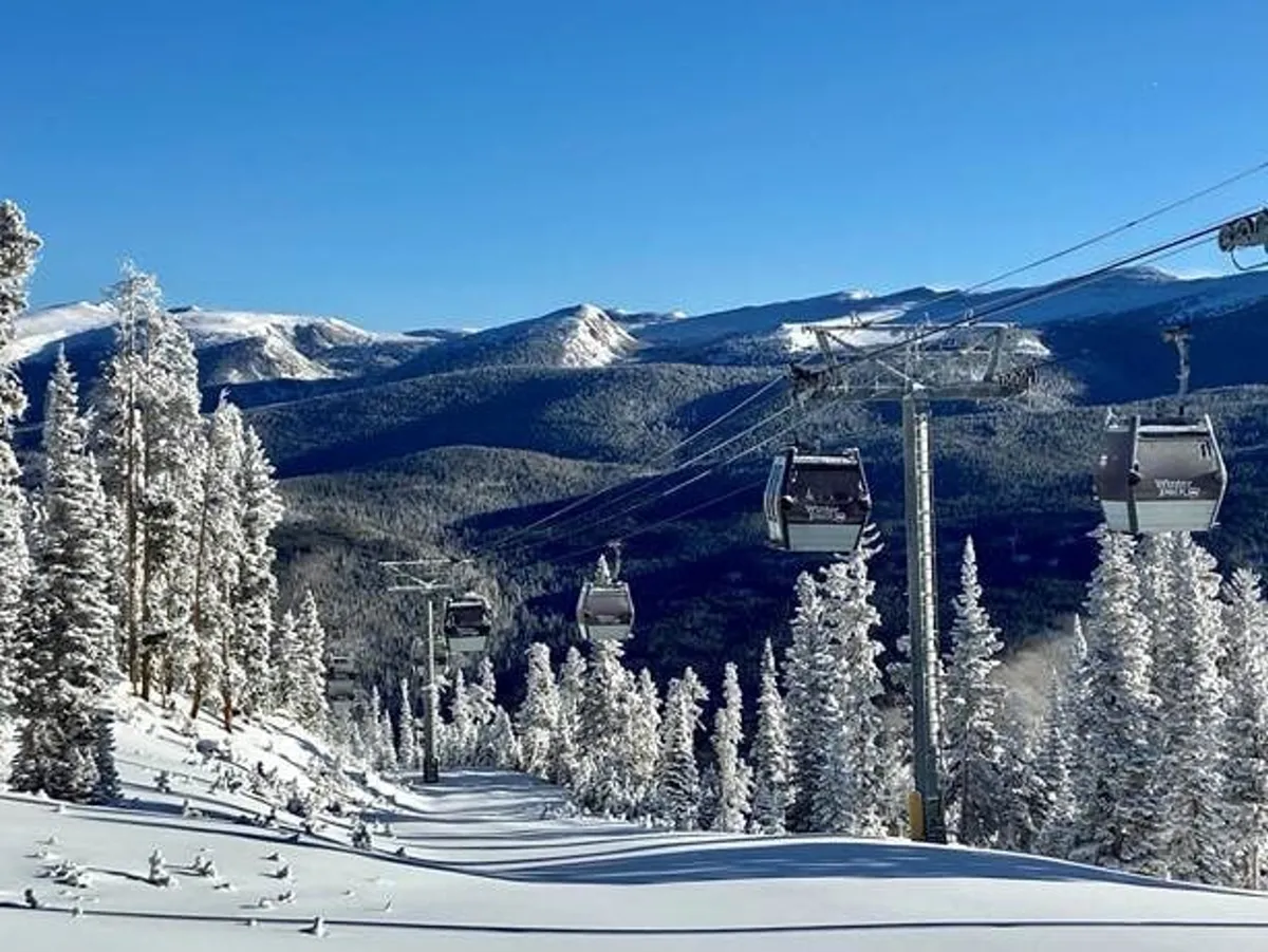 A dynamic outdoor scene featuring a ski lift rising over snow-covered slopes with majestic distant mountains and towering pine trees. The area is bustling with skiers and snowboarders, suggesting active participation in winter sports. The soft glow of sunrise illuminates the landscape, and a lodge at the base hints at communal gathering after a day of adventure.